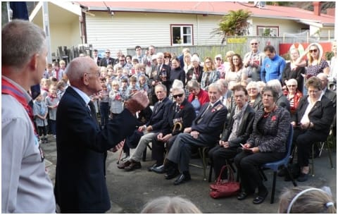 Elderly man addressing seated crowd at memorial event