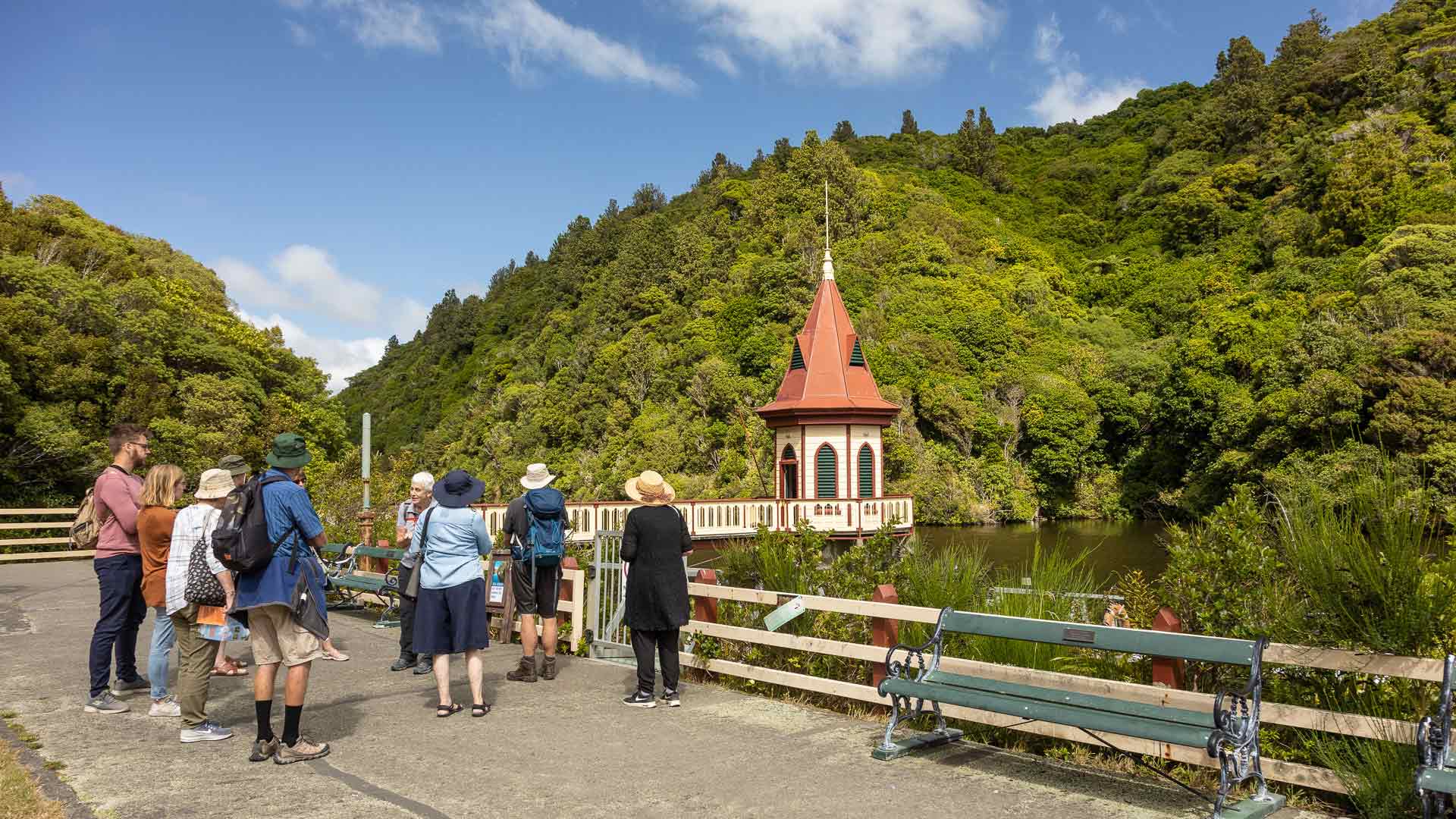 Visitors viewing lakeside pavilion surrounded by lush hills