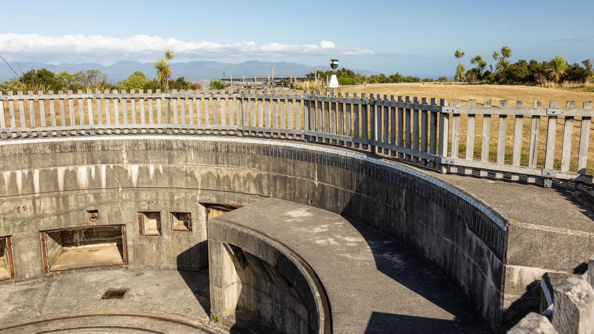 Circular concrete bunker with wooden fence and coastal view