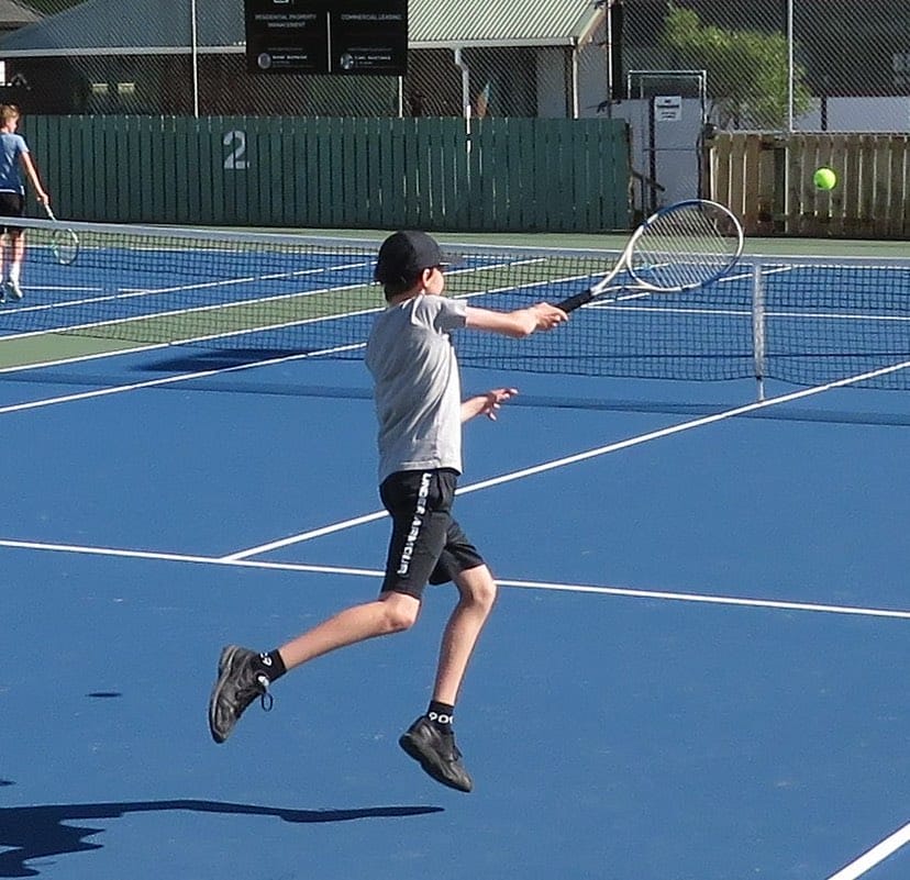 Child jumping to hit tennis ball on court
