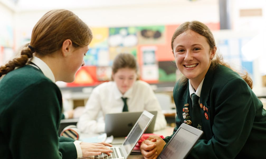 Students in school uniforms using laptops in classroom
